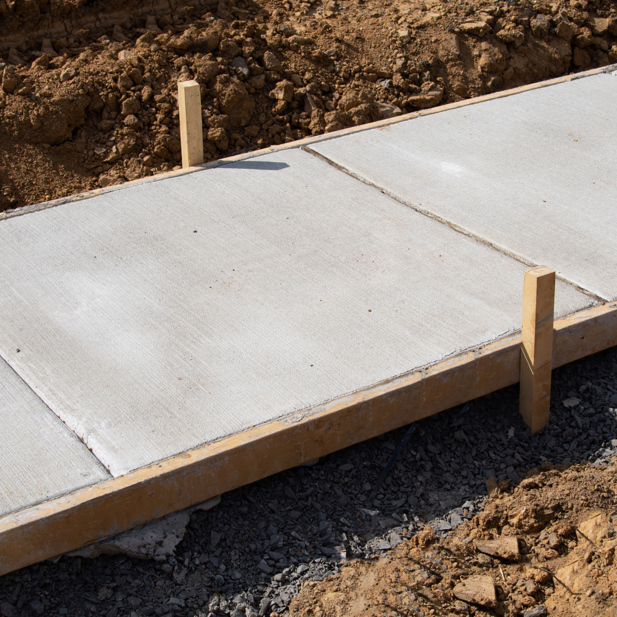 Broom-finished concrete walkway panels separated by tooled joints, set on a compacted stone base